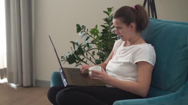 Authentische junge Frau plaudert auf Laptop im Wohnzimmer. Schreiben Suchen mit Hilfe von IT. Happy Lady Arbeiten am Computer Surfen im Internet auf Comfortale Easy Chair. Buisenes, Bildung, Technologiekonzept — Stockvideo