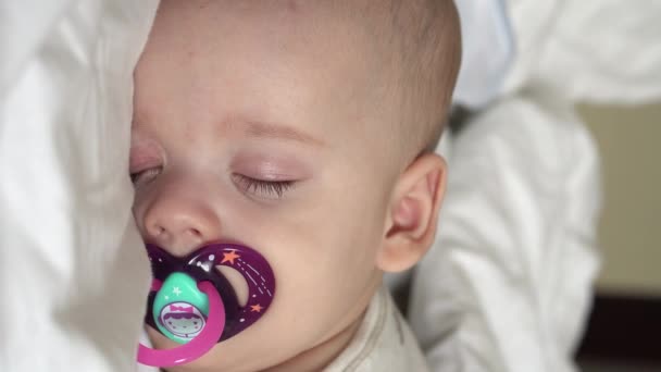 Primo piano verticale viso neonato paffuto bambino addormentato sdraiato sullo stomaco occhi aperti e sorriso coperto di coperta sul letto su sfondo bianco. infanzia, infanzia, sviluppo, medicina e salute. — Video Stock