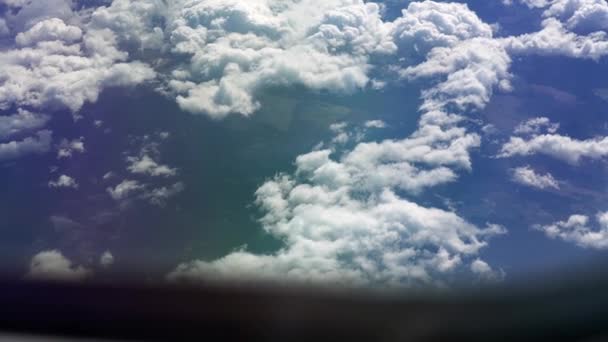 Θέα από το παράθυρο του αεροπλάνου προς το φτερό. Έχει καλό καιρό έξω. Σύννεφα στον ουρανό. Θέα από το φινιστρίνι του αεροπλάνου προς το έδαφος. Πετώντας πάνω από τα σύννεφα ψηλά στον ουρανό. Ο επιβάτης κοιτάει έξω. — Αρχείο Βίντεο