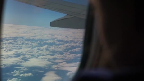 飛行機の玄関前のガラスの上に指で手描きを振っている少女のシルエット、クローズアップスローモーション。飛行機の窓から翼への眺め。空の雲. — ストック動画