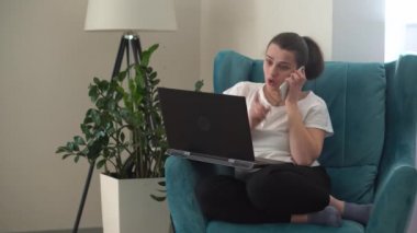 Oturma odasında dizüstü bilgisayarla konuşan otantik bir genç kadın. Kullanarak Yazma Araması. Bilgisayarda çalışan mutlu bayan rahat rahat koltukta interneti tarıyor. Buisenes, Eğitim, Teknoloji Konsepti