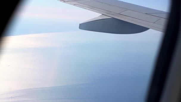 Vue de la fenêtre de l'avion à l'aile. Il fait beau dehors. Nuages dans le ciel. Vue depuis le hublot de l'avion jusqu'au sol. Voler au-dessus des nuages haut dans le ciel. Le passager regarde dehors — Video
