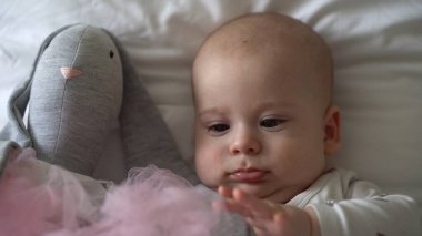 Yakın plan Mutlu neşeli çocuk 6 aylık. Yeni doğan çocuk, beyaz yumuşak yatakta banyo sonrası kameraya bakıyor. Bebek oyuncakla yatmadan önce uyandı. Çocukluk, annelik, aile, bebek konsepti