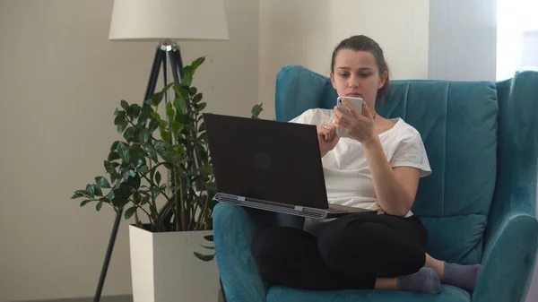 Authentische junge Frau plaudert am Telefon im Wohnzimmer. Schreiben Suchen mit Hilfe von IT. Glückliche Dame, die am Smartphone arbeitet, surft im Internet auf dem bequemen Sessel Easy Chair. Buisenes, Bildung, Technologiekonzept — Stockfoto