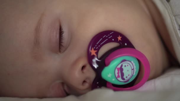 Kojenectví, dětství, vývoj, medicína a zdravotní koncepce - detailní tvář novorozence baculaté spící miminko 6 měsíců s dudlíkem ležícím na břiše přikryté přikrývkou na lůžku na bílém pozadí. — Stock video