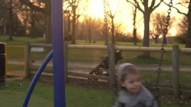 Dışarıda salıncakta sallanırken eğlenen iki küçük kardeşin orta sınıf portresi. Çocuklar kameraya bakıp gülümsüyor. Çocuk parkında oynayan duygusal çocuklar. Mutlu aile, çocukluk.