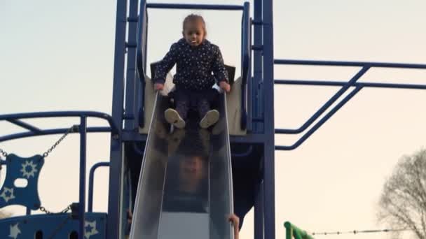 Tři malé Happy Children baví Sliding. Usmívající se kamarádi ze Sourozenců si hrají venku. emocionální děti jezdí na kolotoči na dětském hřišti v parku.Happy rodina, dětství, přátelství — Stock video