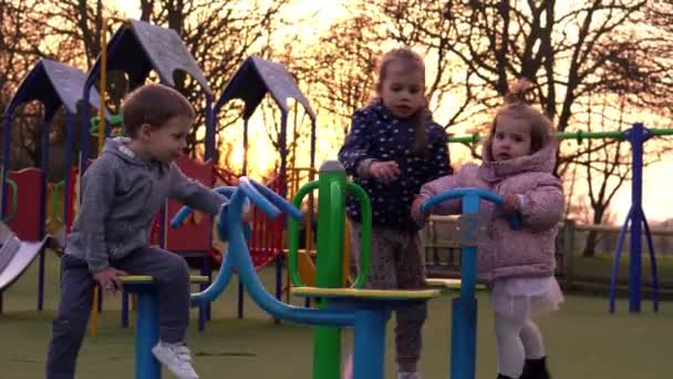 Trójka małych szczęśliwych dzieci bawiących się na karuzeli. Uśmiechnięte rodzeństwo bawi się na zewnątrz. emocjonalne dzieci jeździ na karuzeli w przedszkolu na placu zabaw w Parku.Szczęśliwa rodzina, dzieciństwo — Wideo stockowe