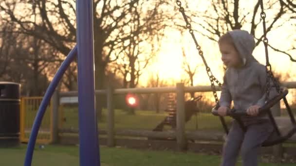 Közepes terv Portré két aranyos kis Siblngs szórakozás Swing kívül. A gyerekek mosolyognak a kamerába. érzelmi gyerekek játszanak játszótéren parkban.Boldog család, gyermekkor — Stock videók
