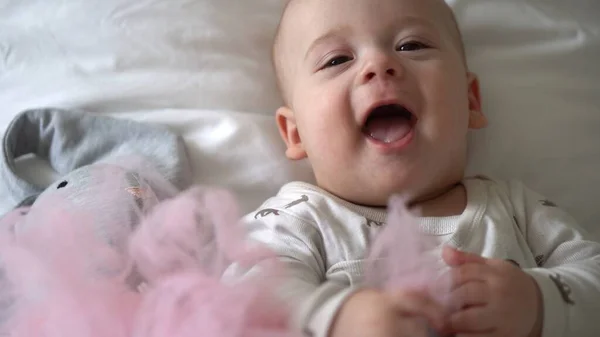 Primo piano Buon bambino giocoso 6 mesi. Ragazzo appena nato guardando la fotocamera dopo la doccia del bagno sul letto morbido bianco. bambino bambino sveglia prima di coricarsi con giocattolo. Infanzia, maternità, famiglia, concetto di bambino — Foto Stock