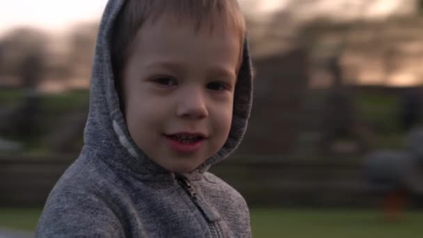 Střední plán Portrét roztomilého chlapečka, který se baví na kolotoči a usmívá se na kameru. emocionální děti jezdí na kolotoči na dětském hřišti v parku.Happy rodina, dětství — Stock video