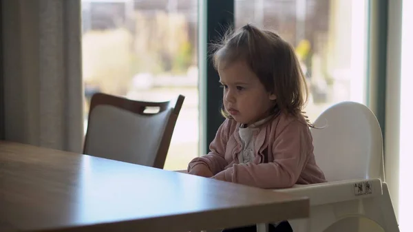 Beyaz sandalyeli küçük bir bebek kendini yemeye çalışıyor. Yüzü yemek lekeli mutlu bir çocuk. Küçük kız kaşıkla yulaf lapası yiyor. Mutfakta kaliteli beslenme kahvaltısı. — Stok fotoğraf