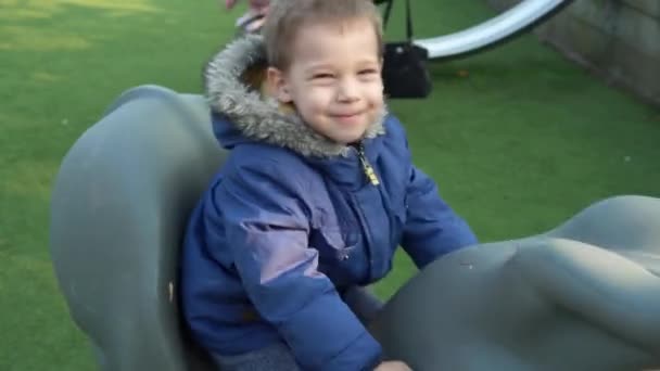 Średni plan Portret jednego uroczego braciszka przedszkolaka bawiącego się na huśtawce na zewnątrz. Dziecko uśmiechnięte patrząc na kamerę bawiącą się na placu zabaw dla dzieci w parku. — Wideo stockowe