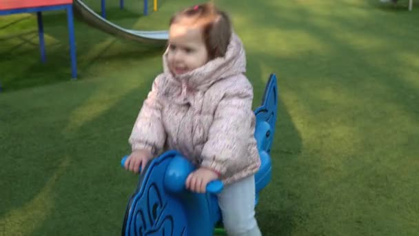 Medium plan Portrait of One cute little Sibling Child preschool girl having fun Swinging On Swing outside. Kid smiling looking at camera playing at children playground in park.Happy family, childhood — Stock Video