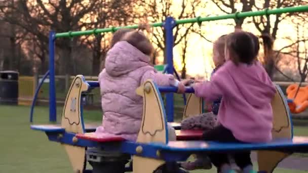 Tre små Happy Children har det sjovt spinning på karrusel-go-round. Smilende søskende venner leger udenfor. følelsesmæssige børn rider på karrusel på legepladsen børnehave i park.Happy familie, barndom – Stock-video