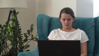 Oturma odasında dizüstü bilgisayarla konuşan otantik bir genç kadın. Kullanarak Yazma Araması. Bilgisayarda çalışan mutlu bayan rahat rahat koltukta interneti tarıyor. Buisenes, Eğitim, Teknoloji Konsepti