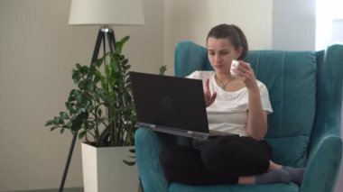 Oturma odasında dizüstü bilgisayarla konuşan otantik bir genç kadın. Kullanarak Yazma Araması. Bilgisayarda çalışan mutlu bayan rahat rahat koltukta interneti tarıyor. Buisenes, Eğitim, Teknoloji Konsepti