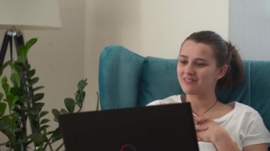 Oturma odasında dizüstü bilgisayarla konuşan otantik bir genç kadın. Kullanarak Yazma Araması. Bilgisayarda çalışan mutlu bayan rahat rahat koltukta interneti tarıyor. Buisenes, Eğitim, Teknoloji Konsepti