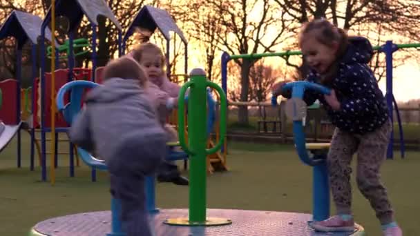 Three little Happy Children having fun spinning on merry-go-round. Smiling Siblings friends playing outside. emotional kids rides on carousel at playground nursery in park.Happy family, childhood — Stock Video