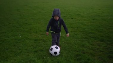 Mutlu çocuk ailesi bahar parkında eğleniyor. Küçük Çocuk Koş. Çocuk Çocuk Yeşil Çimende Siyah Beyaz Klasik Futbol Topu Sürüyor. İnsanlar futbol oynuyor. Çocukluk, Spor, Şampiyonluk Konsepti