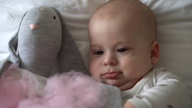 Yakın plan Mutlu neşeli çocuk 6 aylık. Yeni doğan çocuk, beyaz yumuşak yatakta banyo sonrası kameraya bakıyor. Bebek oyuncakla yatmadan önce uyandı. Çocukluk, annelik, aile, bebek konsepti