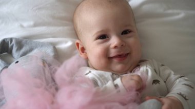 Yakın plan Mutlu neşeli çocuk 6 aylık. Yeni doğan çocuk, beyaz yumuşak yatakta banyo sonrası kameraya bakıyor. Bebek oyuncakla yatmadan önce uyandı. Çocukluk, annelik, aile, bebek konsepti