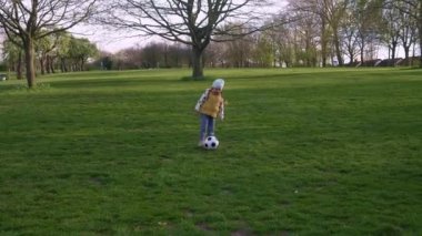 Mutlu çocuk ailesi bahar parkında eğleniyor. Küçük Çocuk Koş. Çocuk Kız Yeşil Çimen Üzerinde Siyah Beyaz Klasik Futbol Topu Sürüyor. İnsanlar futbol oynuyor. Çocukluk, Spor, Şampiyonluk Konsepti