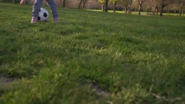 Mutlu çocuk ailesi bahar parkında eğleniyor. Küçük Çocuk Koş. Çocuk Kız Yeşil Çimen Üzerinde Siyah Beyaz Klasik Futbol Topu Sürüyor. İnsanlar futbol oynuyor. Çocukluk, Spor, Şampiyonluk Konsepti