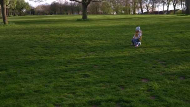 快乐的孩子家庭在春天的公园里玩得开心。小孩儿跑。在绿草上的黑白色经典足球上的童装。人们踢足球。童年、体育、锦标赛概念 — 图库视频影像