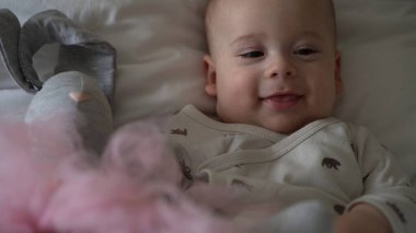 Yakın plan Mutlu neşeli çocuk 6 aylık. Yeni doğan çocuk, beyaz yumuşak yatakta banyo sonrası kameraya bakıyor. Bebek oyuncakla yatmadan önce uyandı. Çocukluk, annelik, aile, bebek konsepti