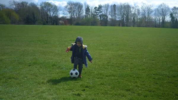 Щасливої сім'ї дітей весняного парку. Маленький хлопчик біжить. Дитячий хлопчик проводить чорну класичну футбольну партію на Зеленій траві. Грає у футбол. Дитинство, спорт, концепція чемпіонату — стокове фото