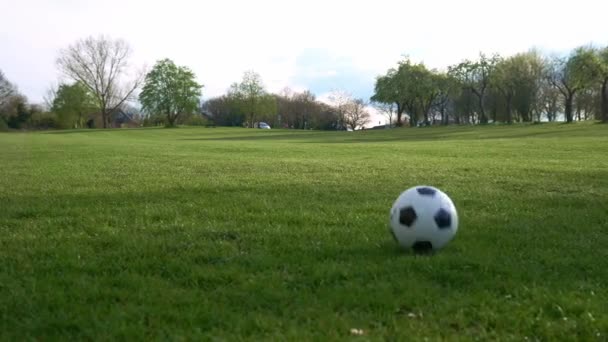 Férfi kék farmerban és mokaszinban, fekete-fehér klasszikus focilabdával zsonglőrködik. Az emberek sportolni járnak. Fiatal fiú focizik. A boldog család csapata a parkban tölti az idejét. Egészséges élet, bajnokság — Stock videók