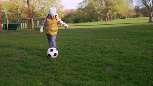 Glückliche Familie von Kindern, die Spaß im Spring Park haben. Kleiner Kinderlauf. Kindermädchen dribbelt schwarzen weißen klassischen Fußballball auf grünem Rasen. Menschen, die Fußball spielen. Kindheit, Sport, Meisterschaftskonzept — Stockvideo