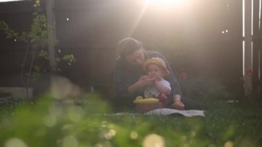Mutlu Genç Neşeli Anne Yeşil Çimlerde Bebek Yiyen Meyveler Tutuyor. Sevimli Anne Bebek Arka Bahçe Bahçesinde Dışarıda Sevgiyle Oynuyor. Ailesi olan küçük çocuk. Aile, Doğa, Ekoloji Kavramı
