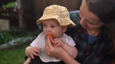 Mutlu Genç Neşeli Anne Yeşil Çimlerde Bebek Yiyen Meyveler Tutuyor. Sevimli Anne Bebek Arka Bahçe Bahçesinde Dışarıda Sevgiyle Oynuyor. Ailesi olan küçük çocuk. Aile, Doğa, Ekoloji Kavramı