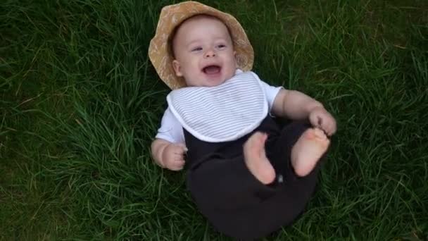 Small Happy Newborn child in summer panama hat Fall down laying on grass barefoot in Summer Sunny Day. Infant Kid Toddler Boy Smilling Face look at camera in Garden ouside Family Childhood Nature — Stock Video