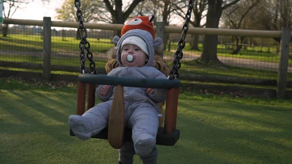 Komik, küçük, tombul kız, ablası, yeni doğmuş erkek kardeşi salıncakta sallıyor. Bebek oyun parkında oynuyor. Çocuk Eğlencesi, Çocukluk, Çocuk Geliştirme, Mutlu Aile Kavramı