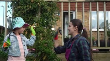 Çocuklu anne ev hanımı iş eldiveni takıyor çiçek dikmek için toprağı hazırlıyor beş kişi de işi bitirip sarılıyor. Çevre Aile Doğası kavramının ekilmesine yardım