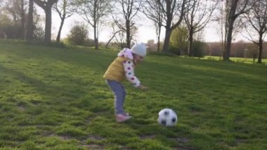 Mutlu çocuk ailesi bahar parkında eğleniyor. Küçük Çocuk Koş. Çocuk Kız Yeşil Çimen Üzerinde Siyah Beyaz Klasik Futbol Topu Sürüyor. İnsanlar futbol oynuyor. Çocukluk, Spor, Şampiyonluk Konsepti