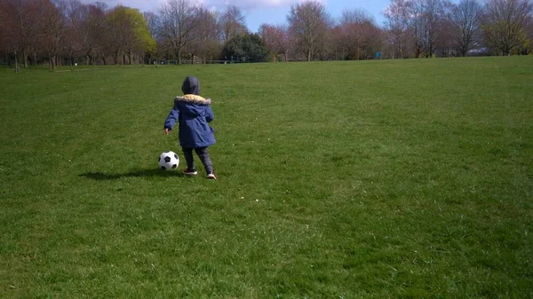 Щасливої сім'ї дітей весняного парку. Маленький хлопчик біжить. Дитячий хлопчик проводить чорну класичну футбольну партію на Зеленій траві. Грає у футбол. Дитинство, спорт, концепція чемпіонату — стокове фото