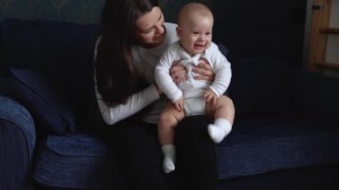 Şefkatli Kafkasyalı Genç Anne, Sevimli Oğlan Bebeği Kucağına Aldı Küçük Çocuğu Kucakladı. Mutlu Uzun Saçlı Anne, Bebek Kızına Kucaklıyor Evdeki Kanepede Oturuyor