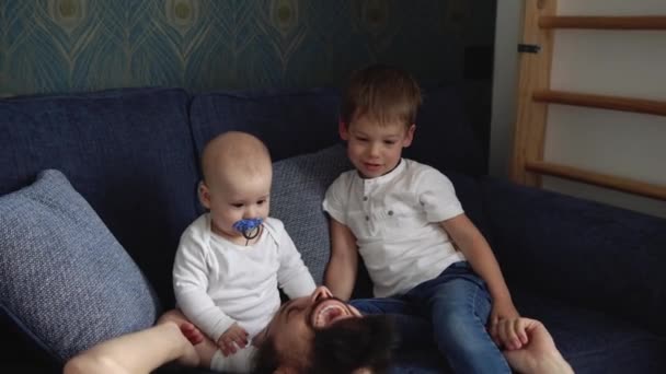 Liefdevolle tedere blanke jonge vader die een schattige schattige baby jongen vasthoudt die kleine jongen omarmt. Gelukkig aanhankelijke lange baard vader knuffelen zuigeling kind meisje dochter zitten op de bank thuis — Stockvideo