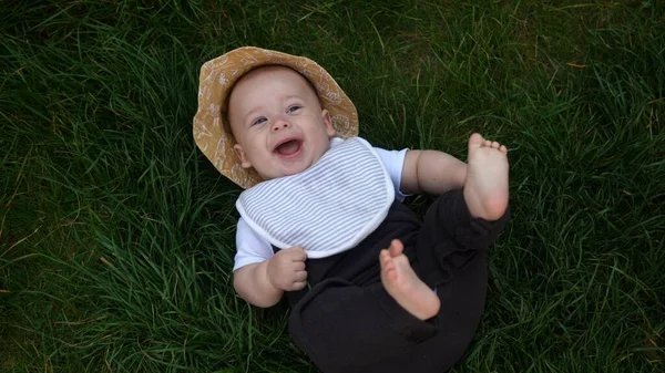 Pequena criança recém-nascida feliz no verão chapéu panama Queda para baixo deitado na grama descalça no dia ensolarado de verão. Infant Kid Criança Menino Smilling Face olhar para a câmera em Garden ouside Família Infância Natureza. — Fotografia de Stock