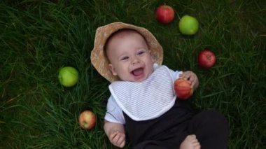 Yaz panama şapkalı mutlu çocuk yaz güneşli yaz gününde çimenlere çıplak ayakla Fresh Fruits Apples ile düşüyor. Bebek Çocuk Yürüyen Çocuk Bahçede Gülümseyen Surat Sağlıklı Yemek Doğa Hasadı