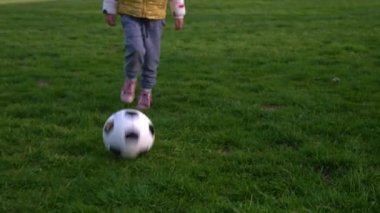 Mutlu çocuk ailesi bahar parkında eğleniyor. Küçük Çocuk Koş. Çocuk Kız Yeşil Çimen Üzerinde Siyah Beyaz Klasik Futbol Topu Sürüyor. İnsanlar futbol oynuyor. Çocukluk, Spor, Şampiyonluk Konsepti
