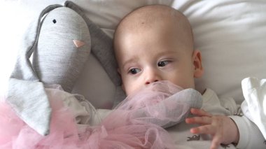 Yakın plan Mutlu neşeli çocuk 6 aylık. Yeni doğan çocuk, beyaz yumuşak yatakta banyo sonrası kameraya bakıyor. Bebek oyuncakla yatmadan önce uyandı. Çocukluk, annelik, aile, bebek konsepti