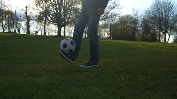 Man in blauwe jeans en sporadisch jongleren met zwart-wit klassieke voetbal bal. Mensen gaan naar de sportschool. Jonge jongen die voetbal speelt. Happy Family Team hebben tijd doorgebracht in het park. Gezond leven, kampioenschap — Stockfoto