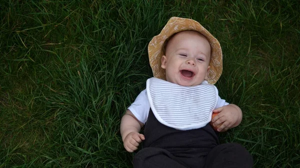 Small Happy Newborn παιδί το καλοκαίρι panama καπέλο Πτώση κάτω στο γρασίδι ξυπόλυτη το καλοκαίρι Sunny Day. Βρέφος Παιδί Βρέφος Boy Saling Face ματιά στην κάμερα στο κήπο ouside Οικογένεια Παιδική Φύση. — Φωτογραφία Αρχείου