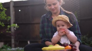 Mutlu Genç Neşeli Anne Yeşil Çimlerde Bebek Yiyen Meyveler Tutuyor. Sevimli Anne Bebek Arka Bahçe Bahçesinde Dışarıda Sevgiyle Oynuyor. Ailesi olan küçük çocuk. Aile, Doğa, Ekoloji Kavramı