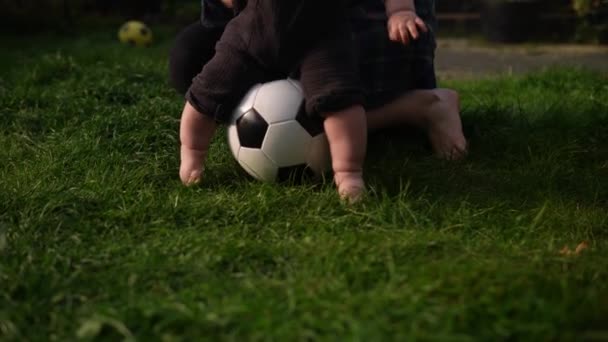 Feliz bebê sentado com futebol preto branco clássico bola na grama verde. Adorável bebê infantil brincando ao ar livre no jardim do quintal. Filhinhos com pais. Futebol, Campeonato, Conceito de Esporte — Vídeo de Stock